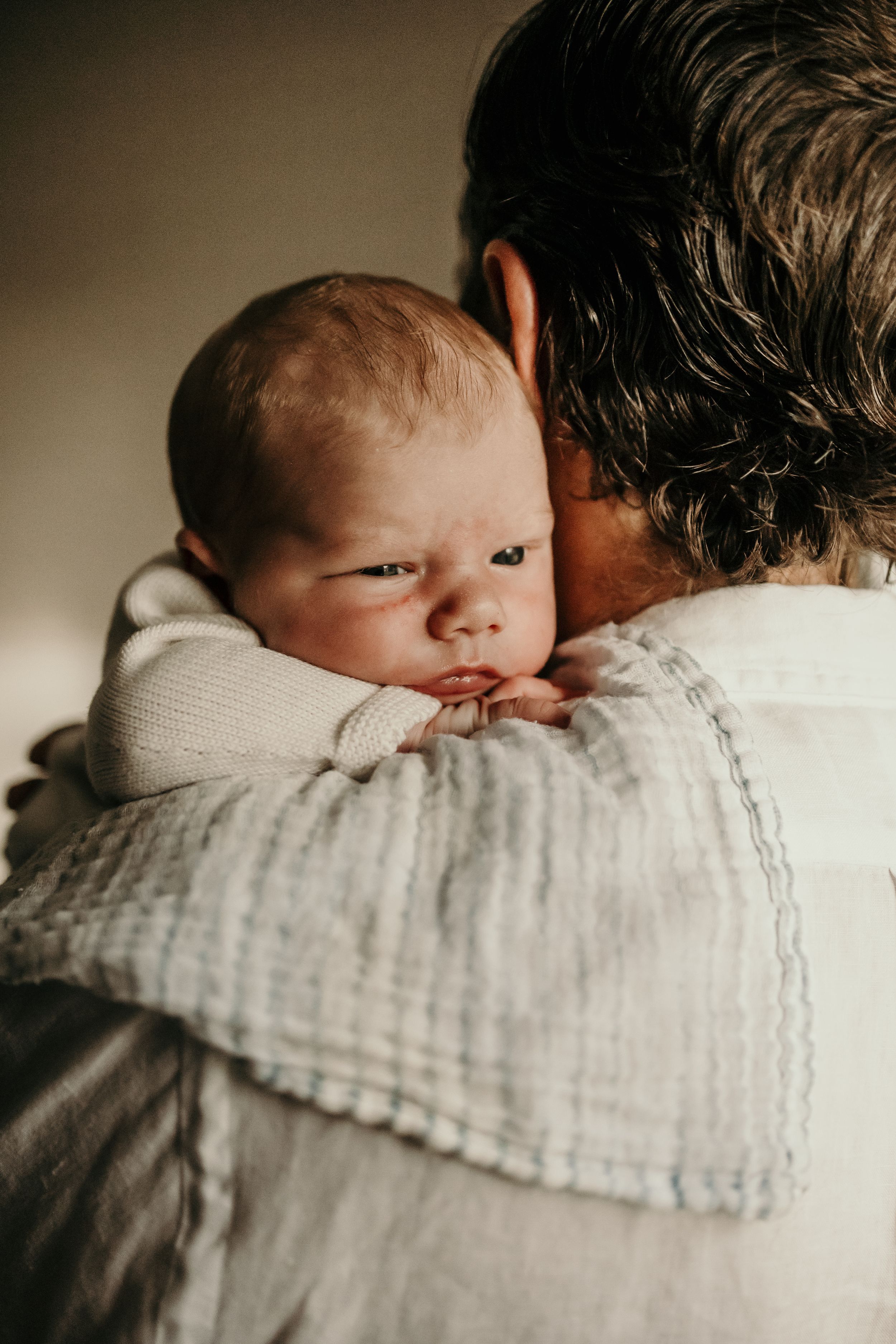 A series of intimate photos showing a sleeping newborn baby swaddled in soft white muslin fabric against a neutral background.