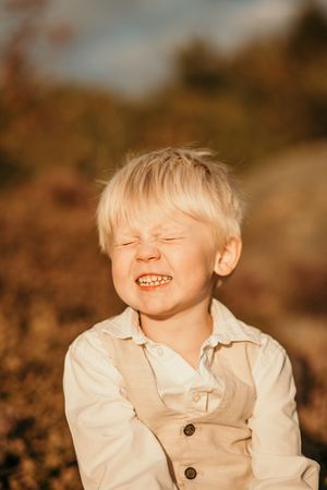 A child in a white button-down shirt laughs joyfully while playing outdoors in warm autumn lighting.