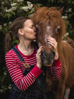 Person in red striped shirt shares an intimate moment with brown pony among spring blossoms.