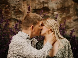 Romantic kiss among purple flowers against stone wall background.