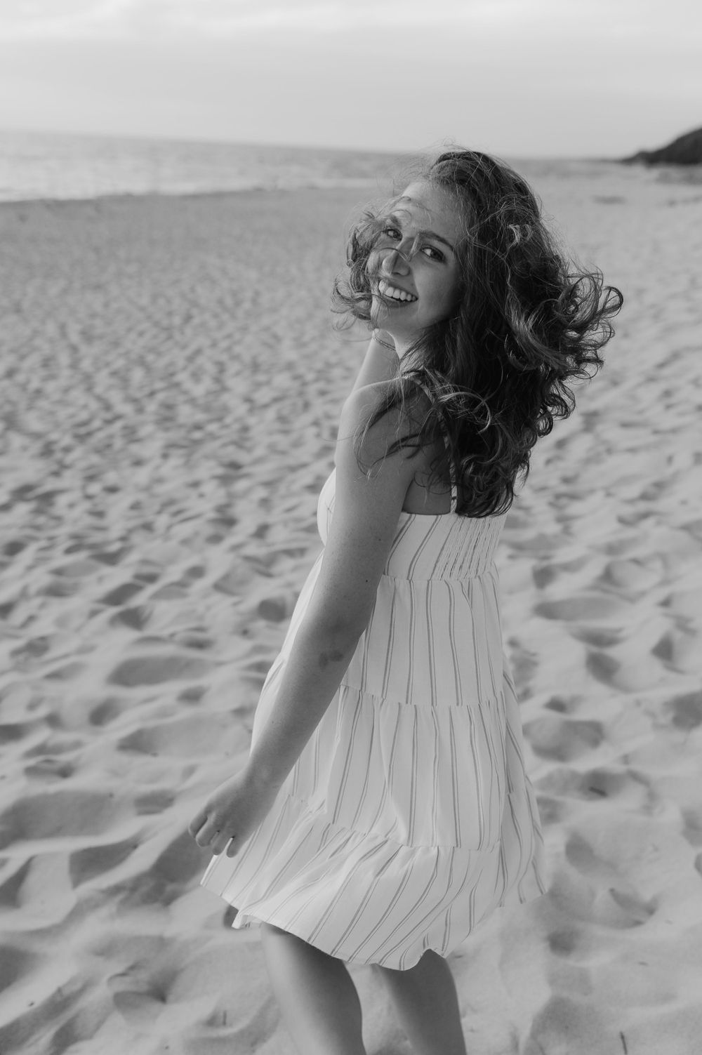 Carefree black and white portrait in a flowy white dress on a sandy beach.
