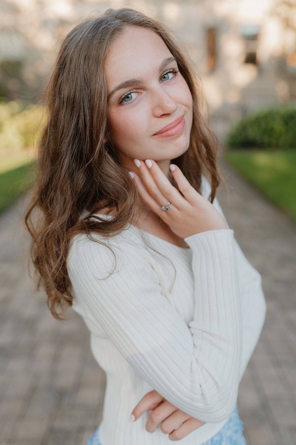 Soft natural portrait in a cozy white sweater against a garden background.
