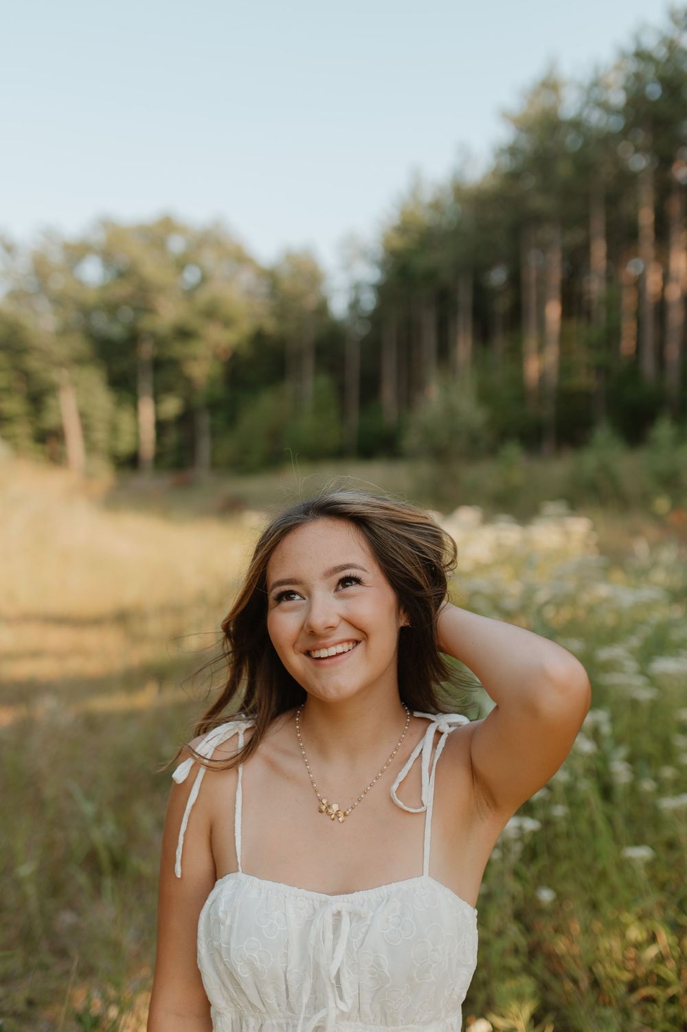 Woman in white sundress smiling joyfully in golden summer meadow.