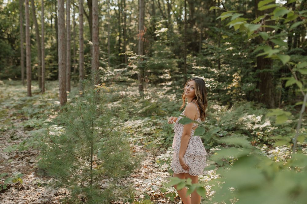 Young woman in light dress walking through sunlit forest clearing.