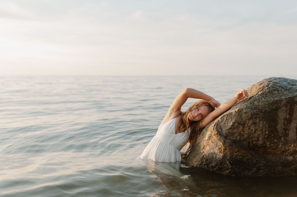 Artistic beach photo with someone lounging on a rock by the ocean at sunset.