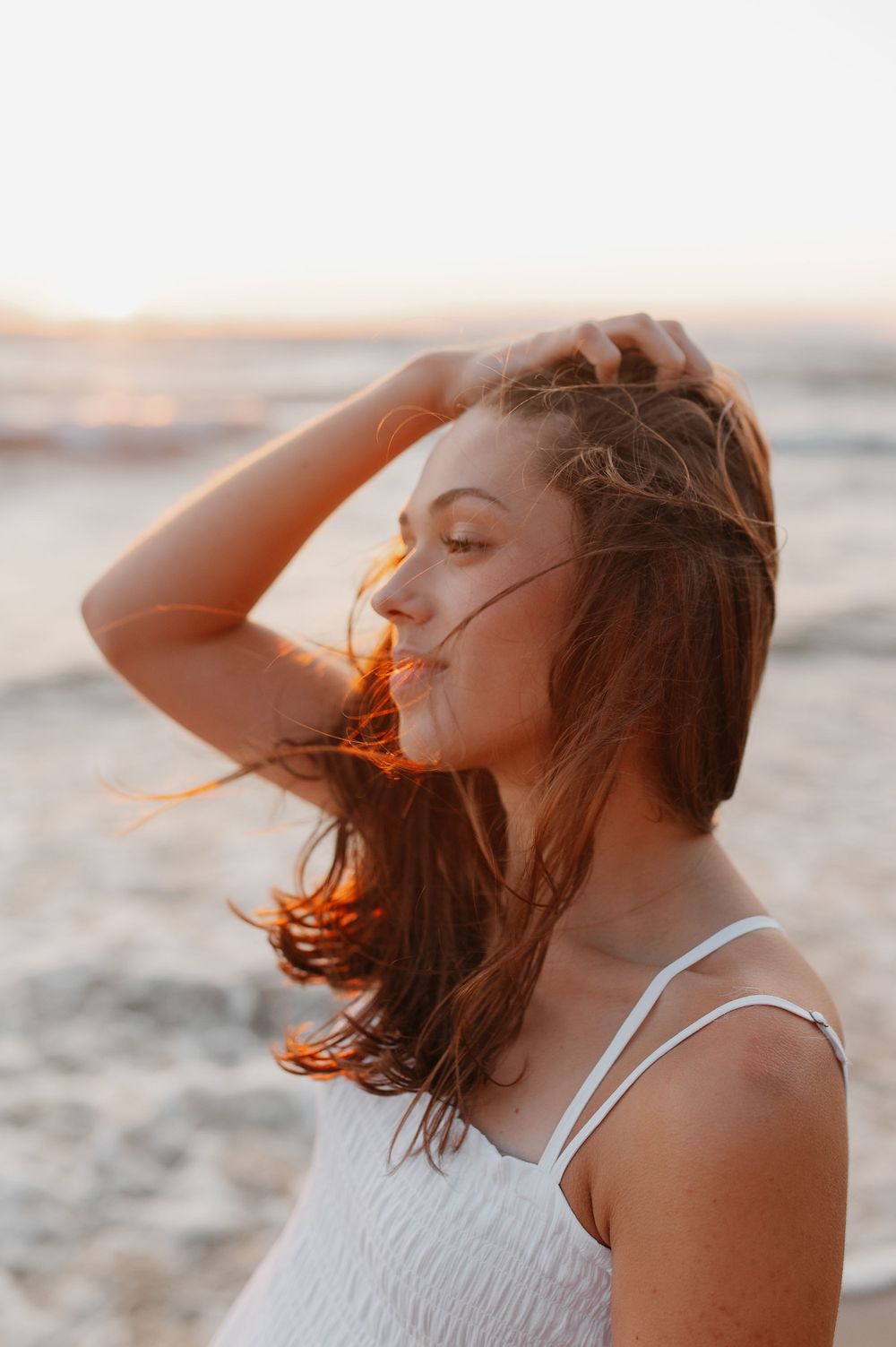 A serene beach portrait captures windswept hair glowing in golden sunset light.