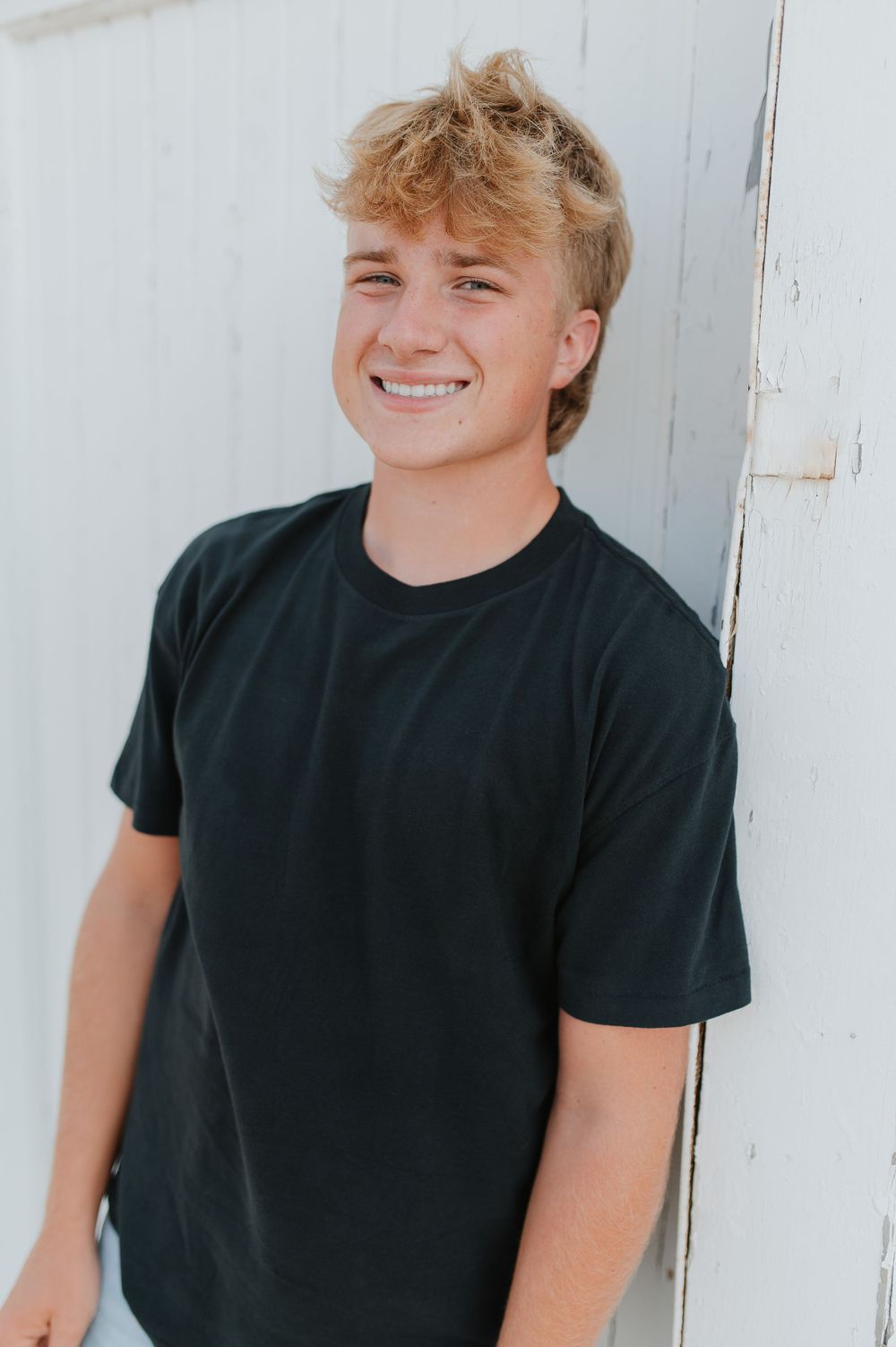 Portrait against white wall showing person in black t-shirt with natural expression.