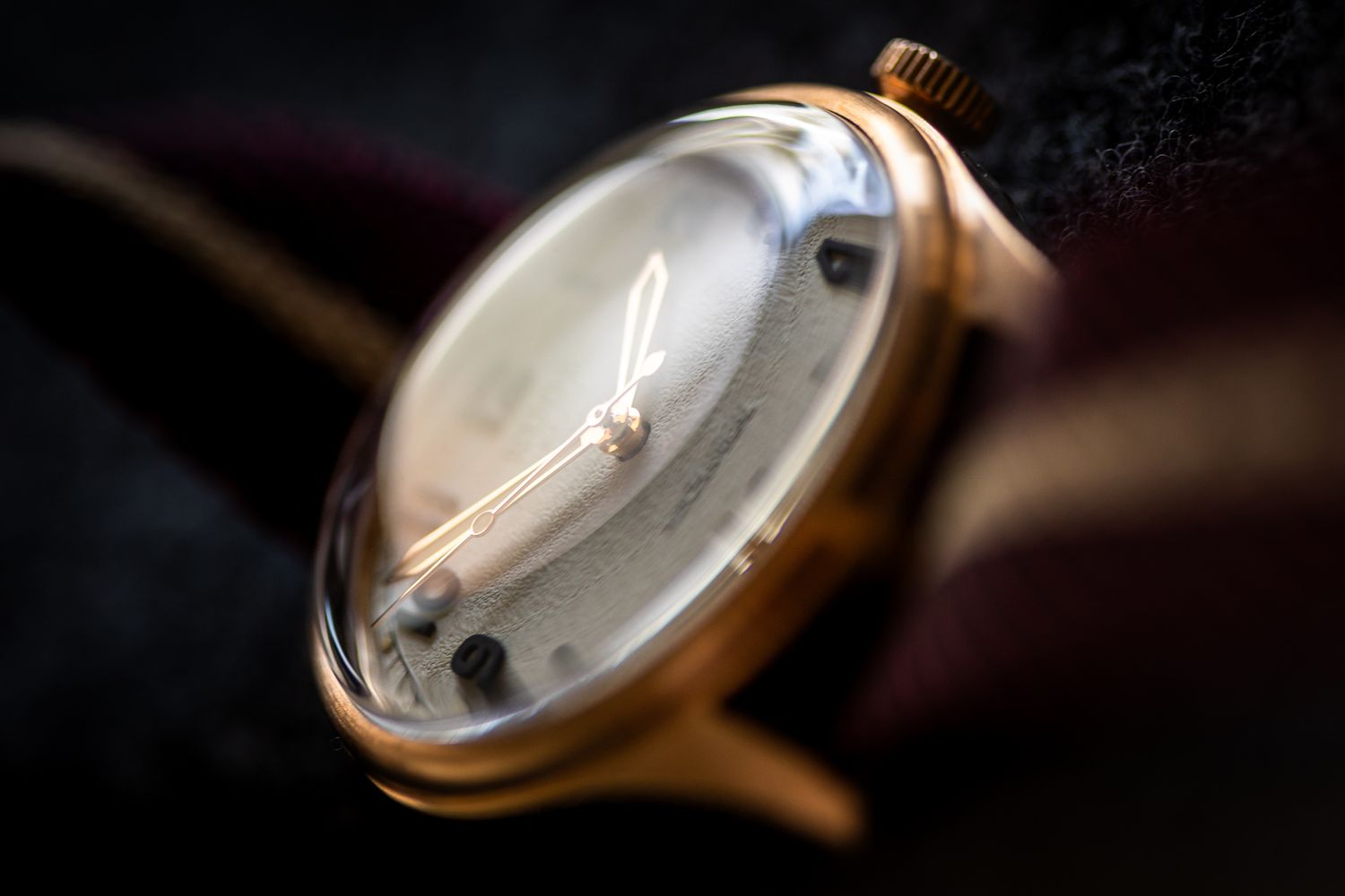 Closeup shot of a vintage gold wristwatch face with elegant hands against dark background.