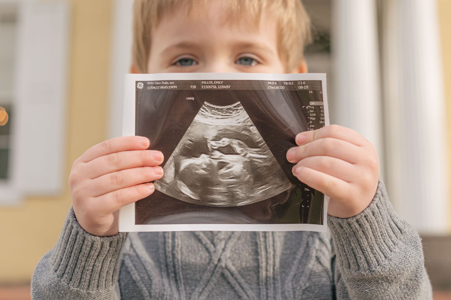 Child holding up an ultrasound image showing a clear view of a baby.