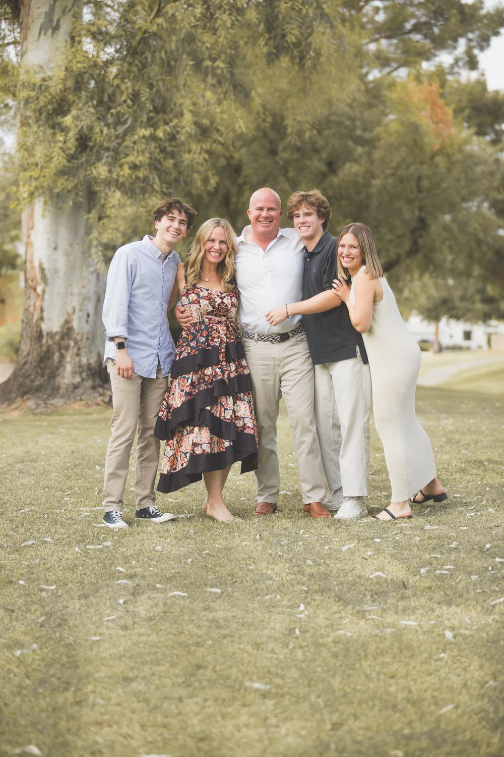 A group of people pose together on a grassy lawn during a sunny outdoor photo session.