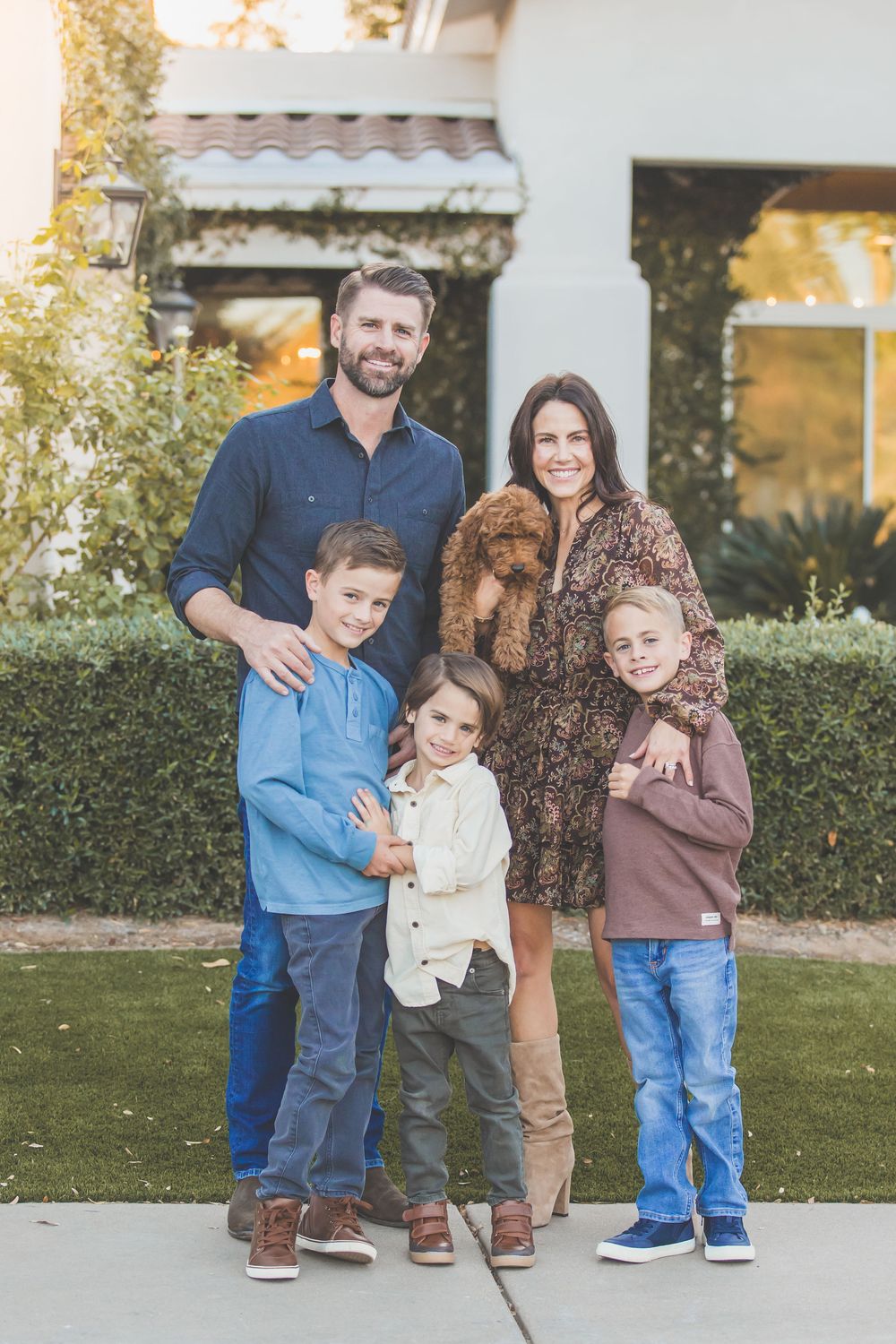 A casual family group stands together outdoors in coordinated blue and brown outfits during an autumn photoshoot.