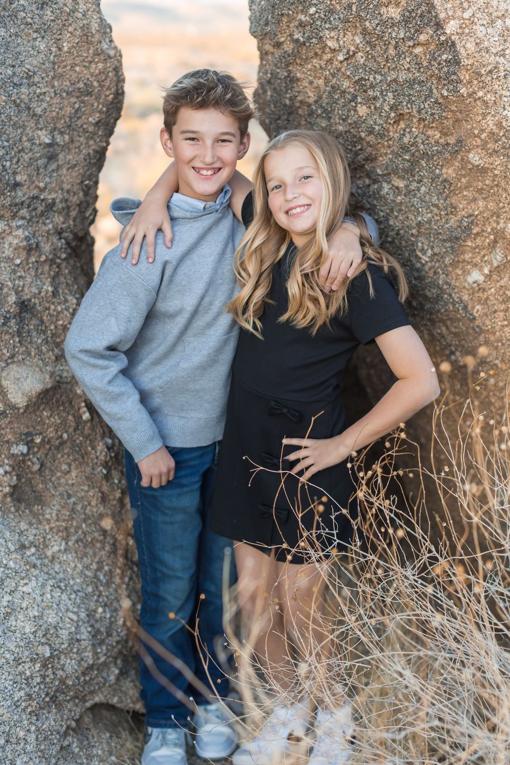 Two people pose playfully against a large granite rock formation in casual attire.