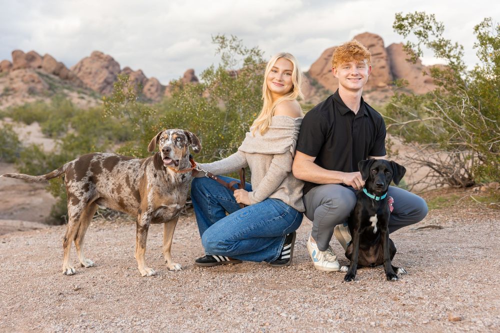 Family sits together with their dogs on rocky desert terrain during outdoor photoshoot.