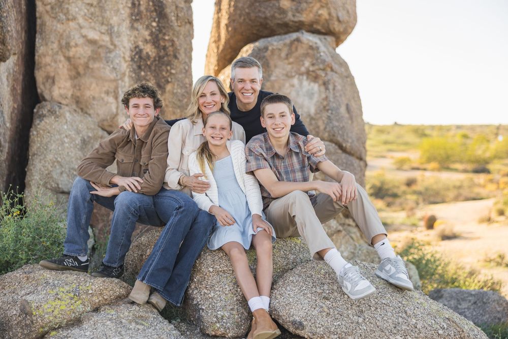 A family sits together on large desert rocks during a golden hour photoshoot in an arid landscape.