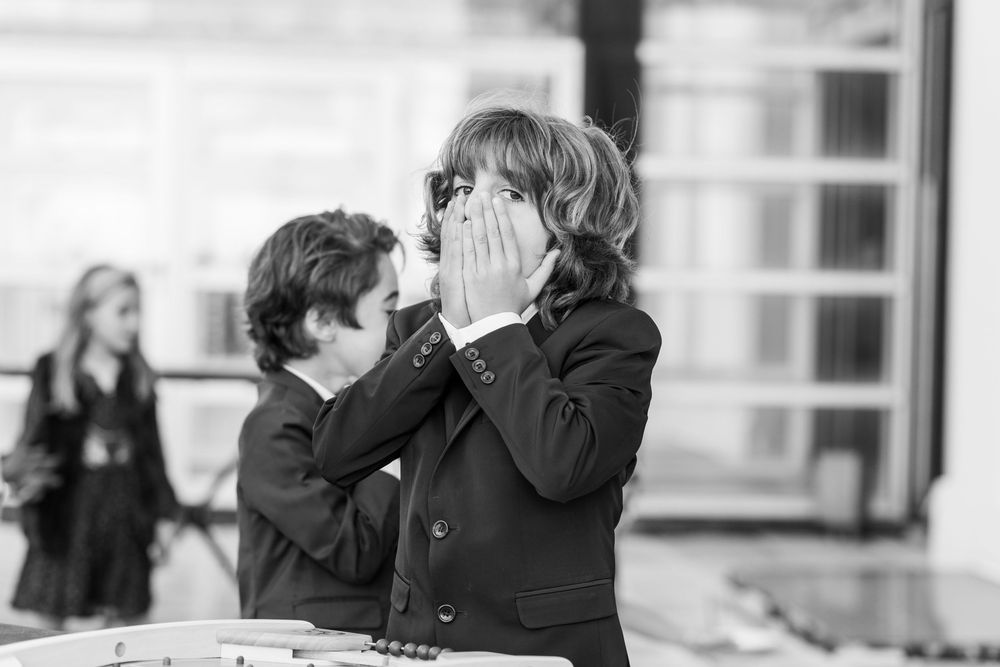 Enfant en noir et blanc couvrant son visage en jouant, moment spontané et naturel capté sur le vif.