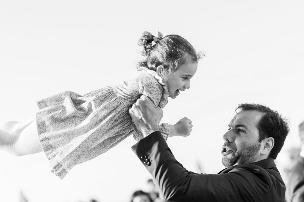 Enfant souriant dans les bras d’un adulte en noir et blanc, moment tendre et complice.