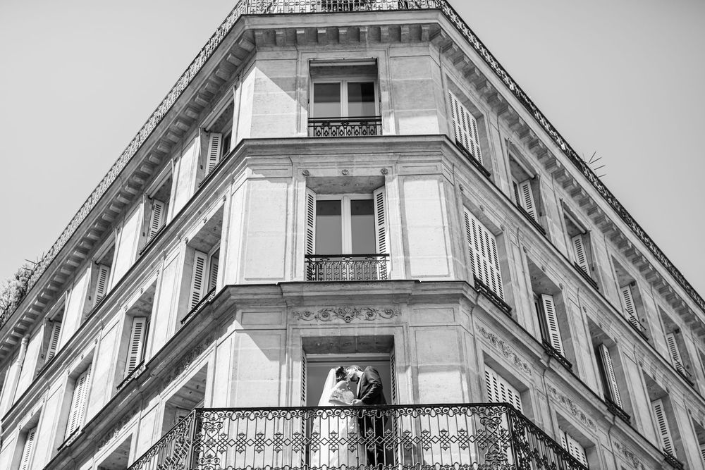 Couple apparaissant à une fenêtre d’un immeuble parisien haussmannien, scène urbaine et romantique. Couple d'un mariage juif.