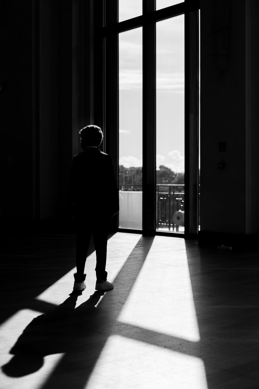 Silhouette d’un bar mitzvah debout près d’une grande baie vitrée, lumière douce et ombres graphiques. Casino de Biarritz.