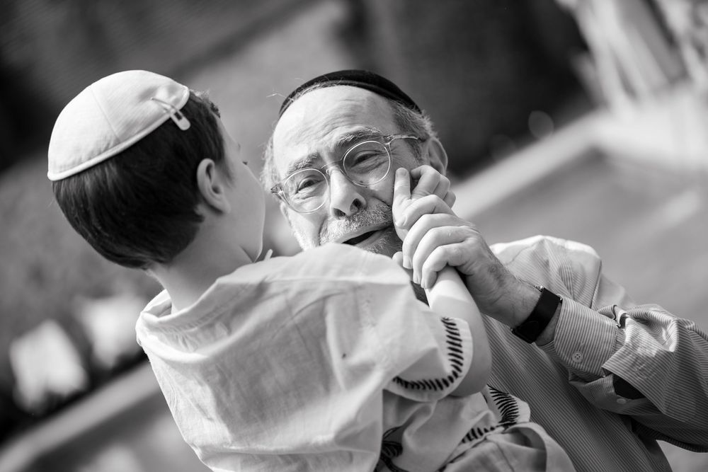 Père et fils en noir et blanc partageant un moment tendre, regard complice et émotion authentique lors d'une bar mitzvah.