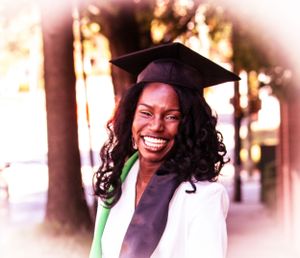 Graduate in cap and white gown smiles joyfully during outdoor graduation photoshoot.