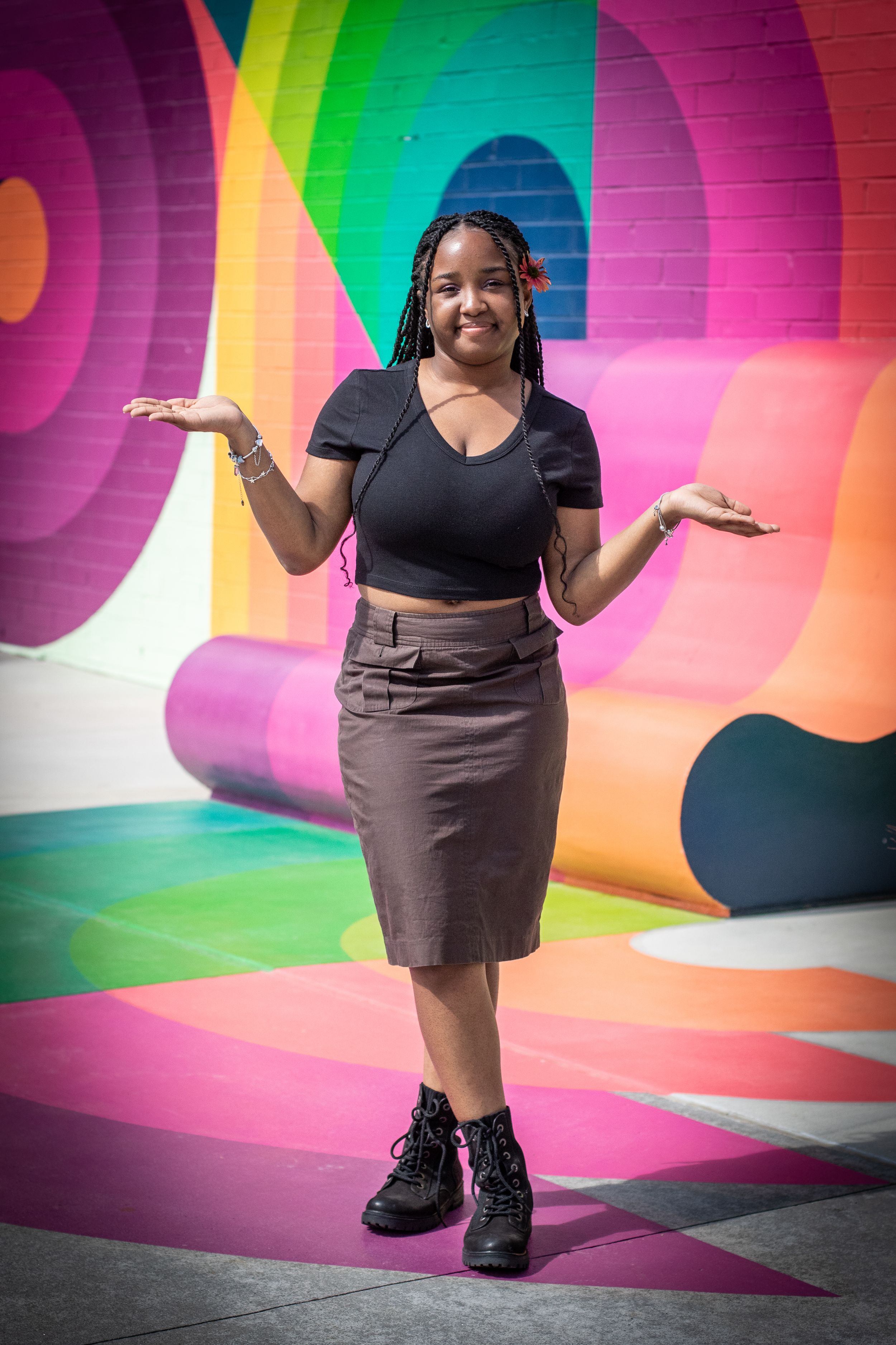Portrait against vibrant rainbow wall mural showing casual urban style and expressive pose.