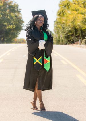 Graduate wearing cap and gown with Jamaica flag stole poses on outdoor road.
