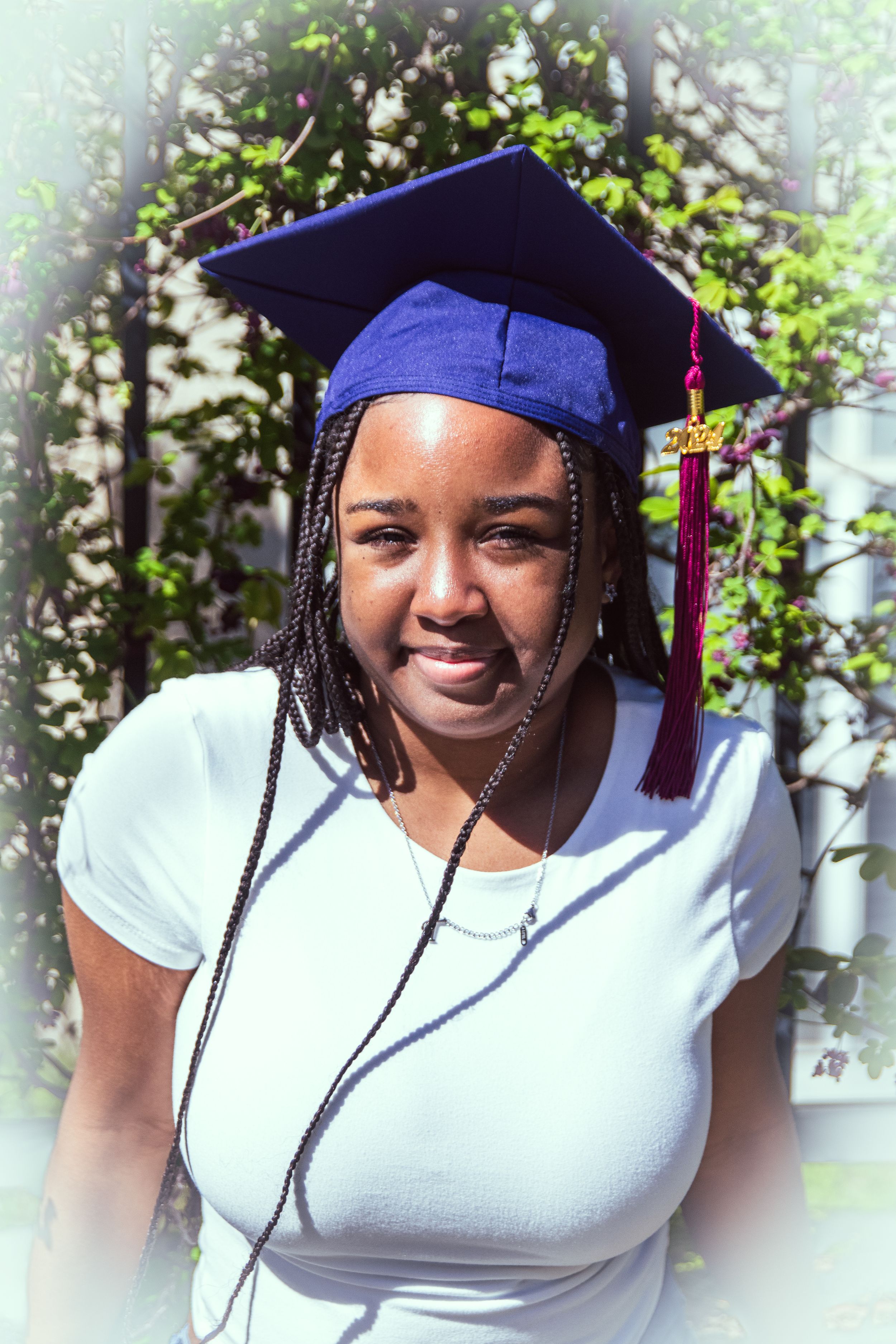 Graduation portrait outdoors featuring blue cap with tassel and natural garden background.