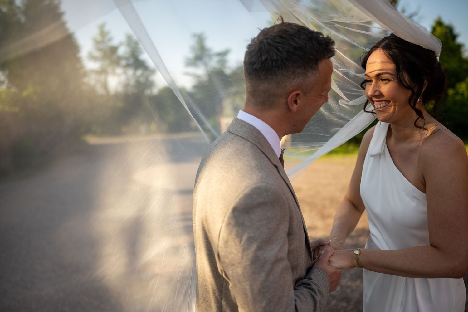 A romantic wedding couple shares an intimate moment in a sunlit garden setting with glowing backlight.