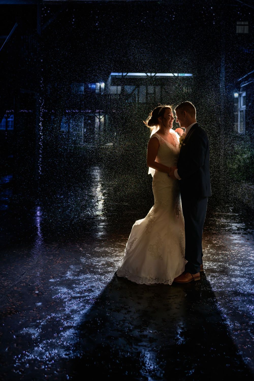 A couple in formal attire dances together in a dark outdoor setting illuminated by soft lighting.