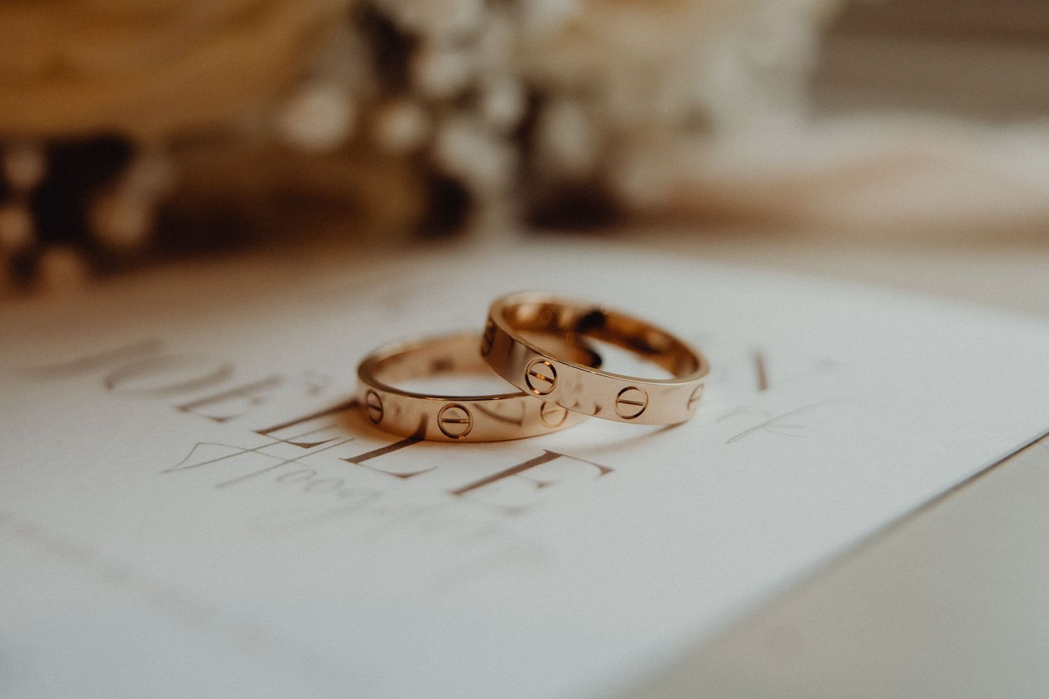 Close-up of two gold wedding bands with delicate engravings on white paper.