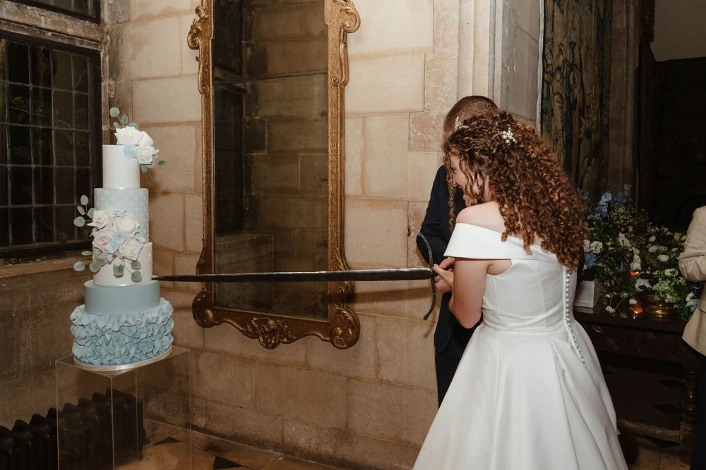 Berkeley Castle wedding venue Gloucestershire medieval castle evening reception main hall bride and groom cutting cake with sword
