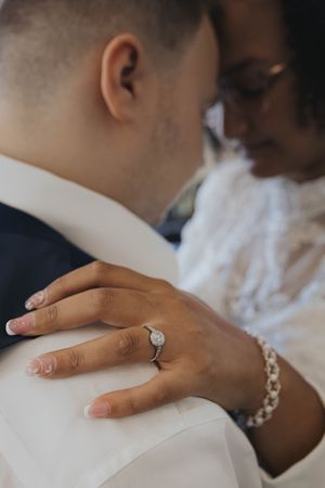 Close-up of hands wearing engagement ring and wedding band against white fabric background.