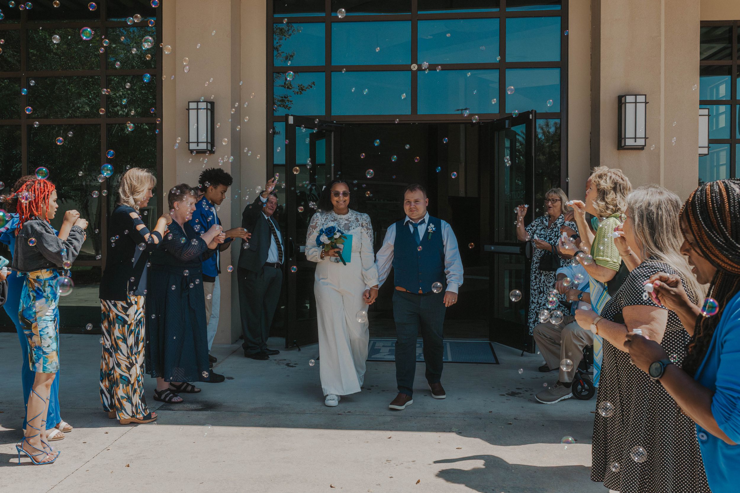 Wedding guests gather outside a venue with teal-colored doors while taking photos and socializing.