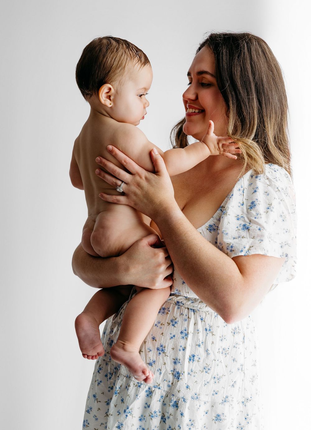 A parent in a floral dress shares tender moments with their baby against a white background in a photo series.