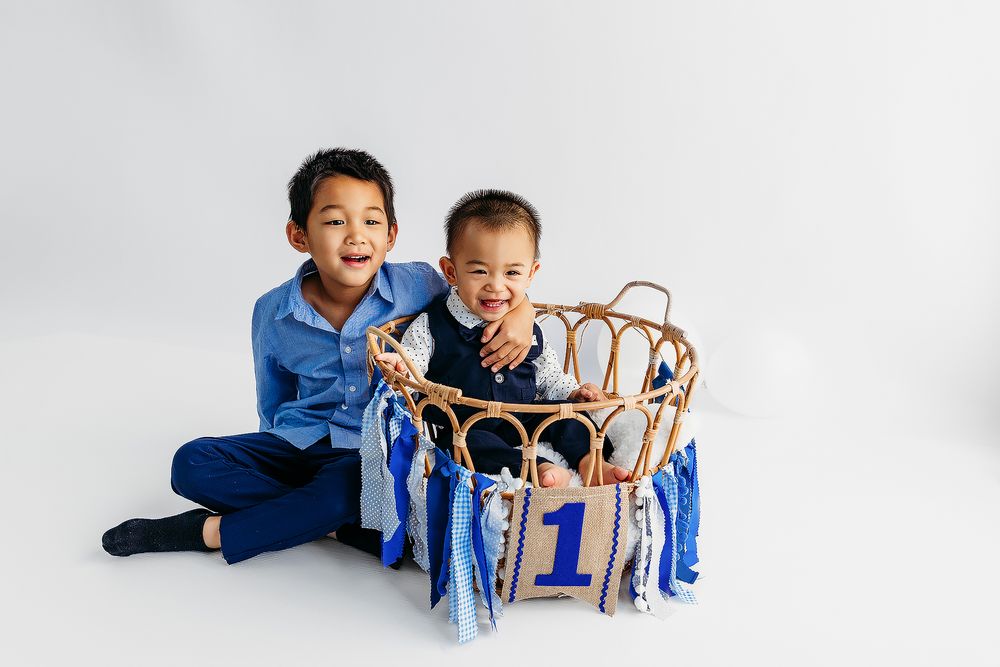 Two children in matching blue outfits play with a wooden toy train set on a light colored floor.
