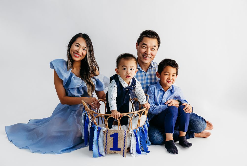 Family wearing coordinated blue outfits poses together on white backdrop for professional portrait session.