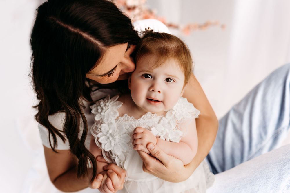 A joyful moment shared between parent and baby in delicate white lace outfits. in Fairfax, VA