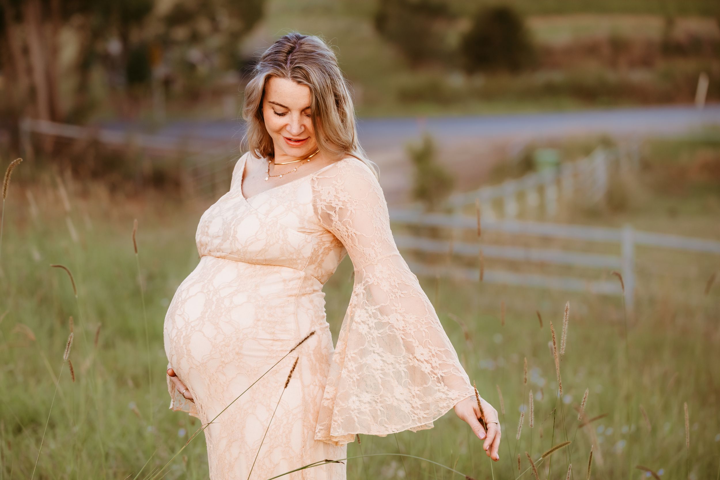 Pregnant woman in lace dress cradling baby bump in golden field.