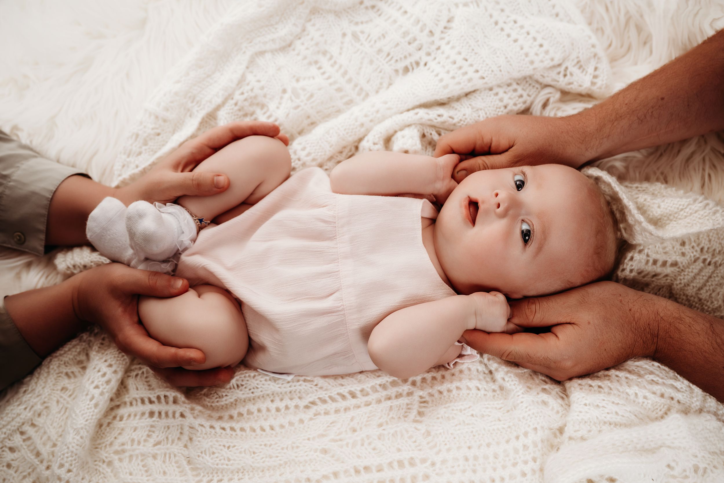 A series of tender moments captured between parent and baby lying on white textiles in soft natural light.