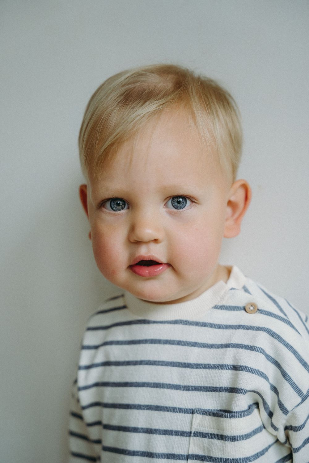 Young toddler in striped shirt smiles against neutral background.