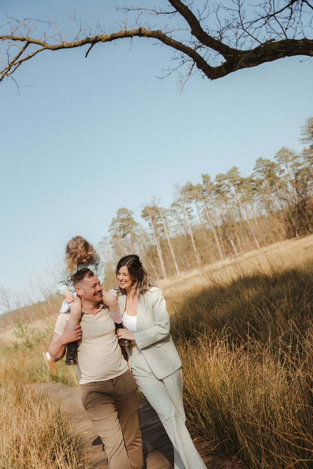 Family enjoying outdoor moment together in tall grass field with pine trees.