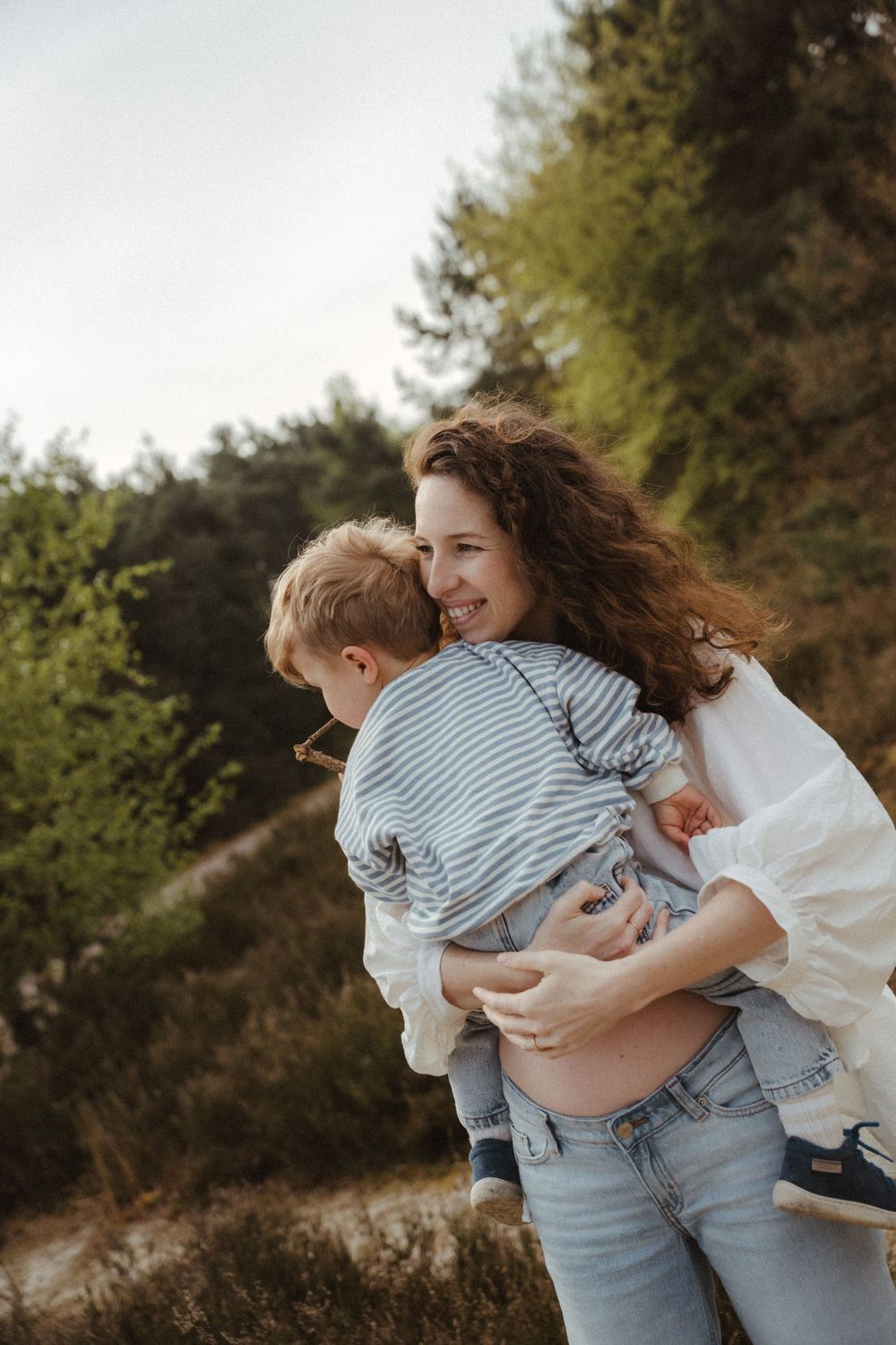 Mother and child share joyful moment outdoors against natural forest backdrop.
