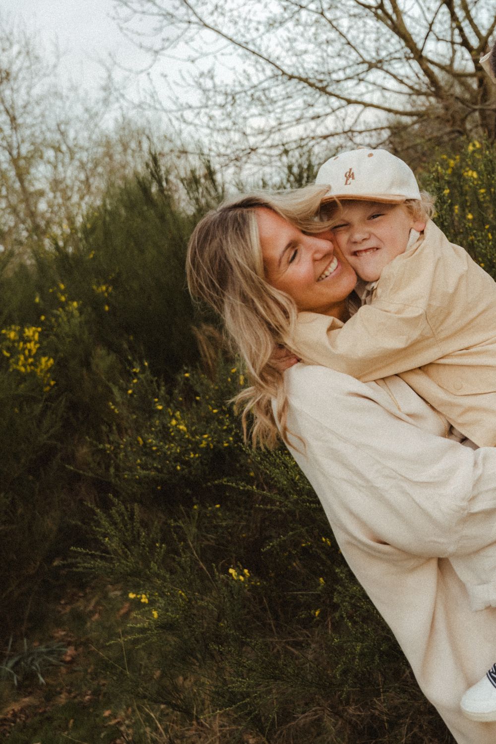 Parent and child embrace outdoors among blooming yellow wildflowers at sunset.