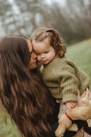 Tender moment between parent and child with stuffed animal on a cloudy day.