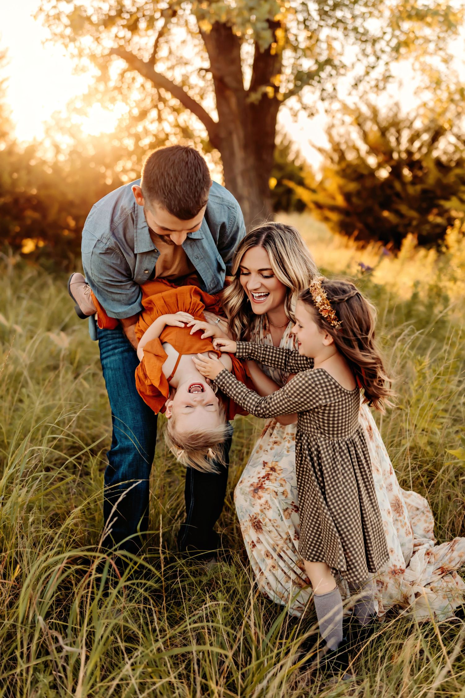Family playing and laughing together in tall grass during golden hour sunset photoshoot.