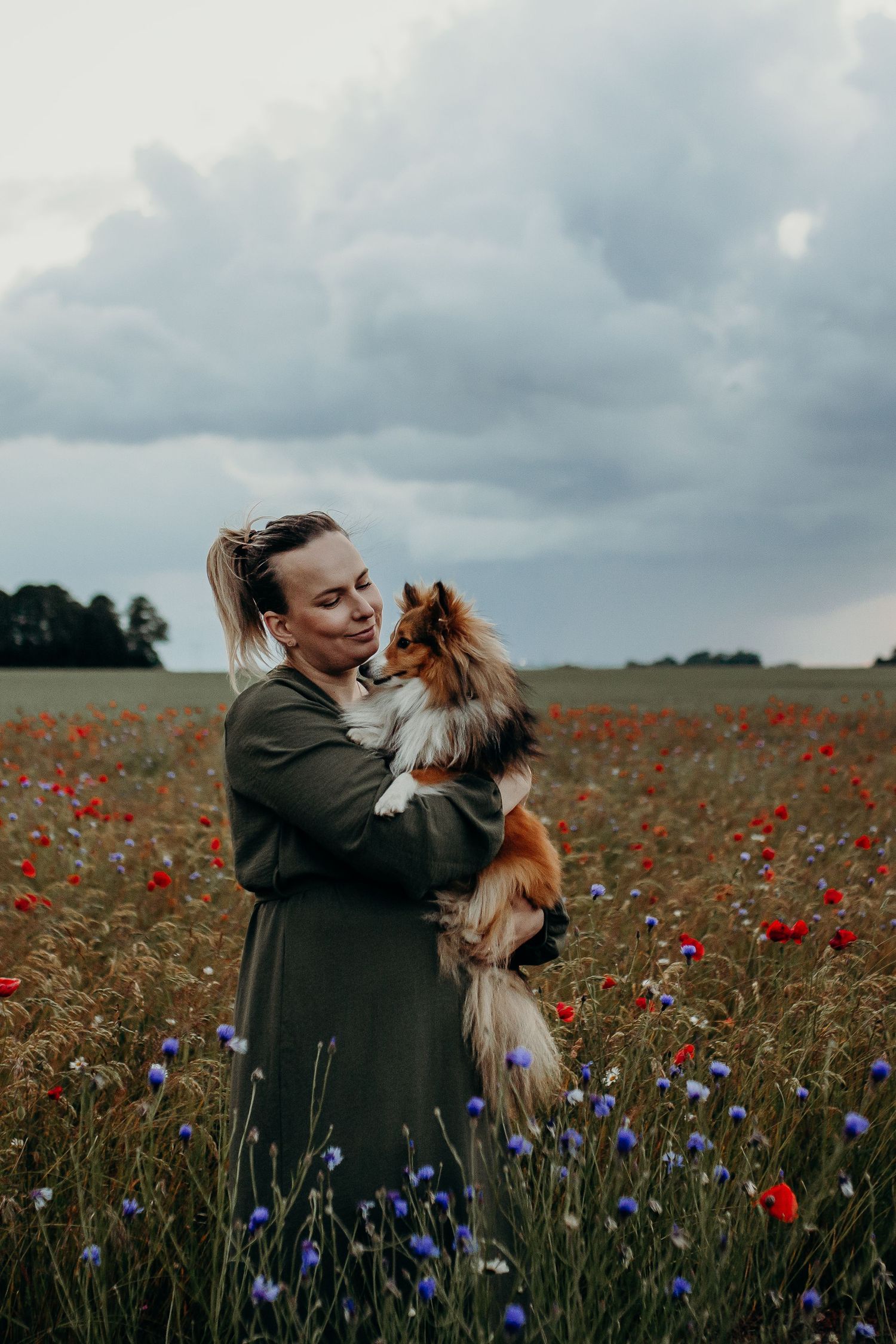 gravidfotograf som står i ett vallmofält med sin hund i famnen