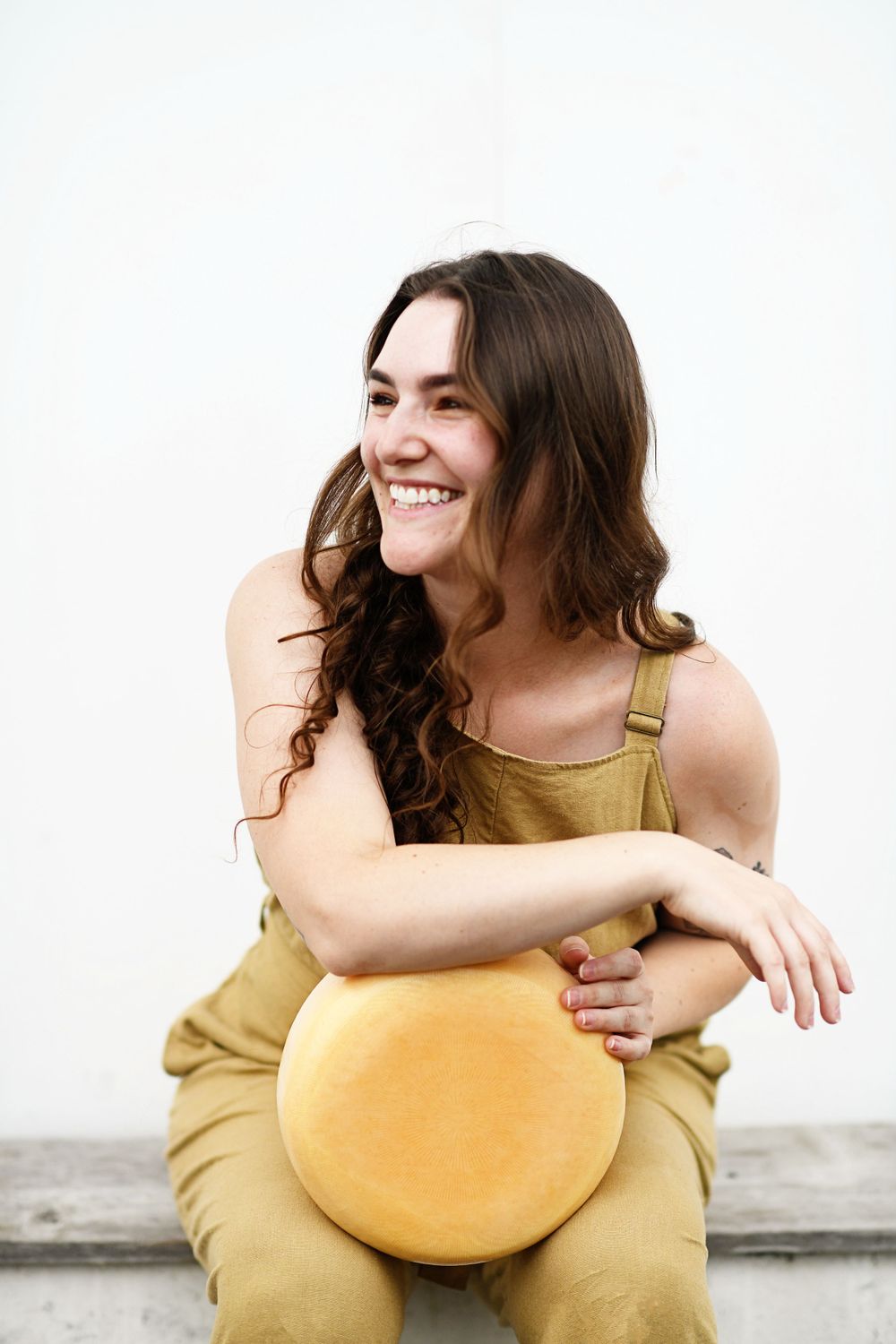 Person in yellow overalls sitting casually and laughing while holding a round yellow cushion.
