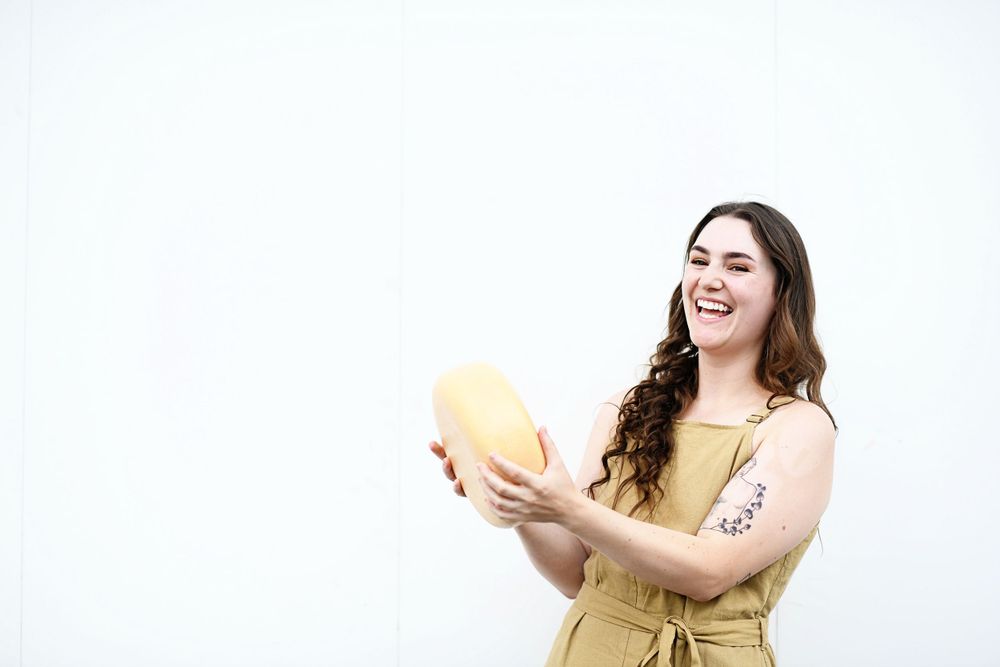 Woman in yellow dress laughs while holding cantaloupe against white background.