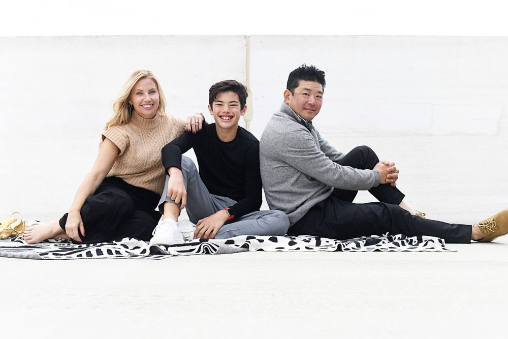 Family sitting together on patterned blanket against white background.