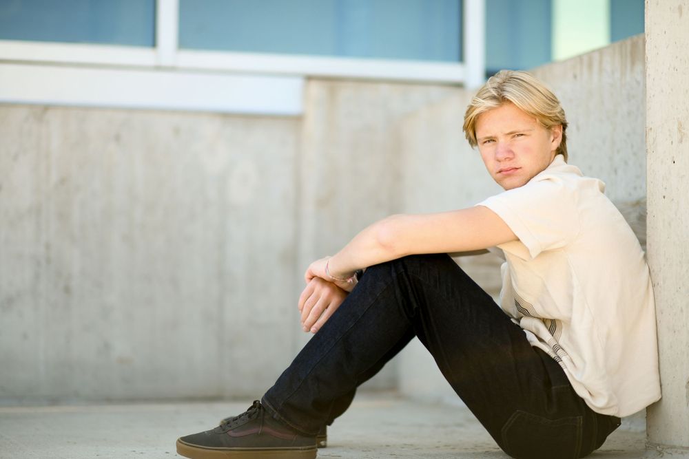 Person sitting on concrete floor wearing white shirt and dark pants in contemplative pose.